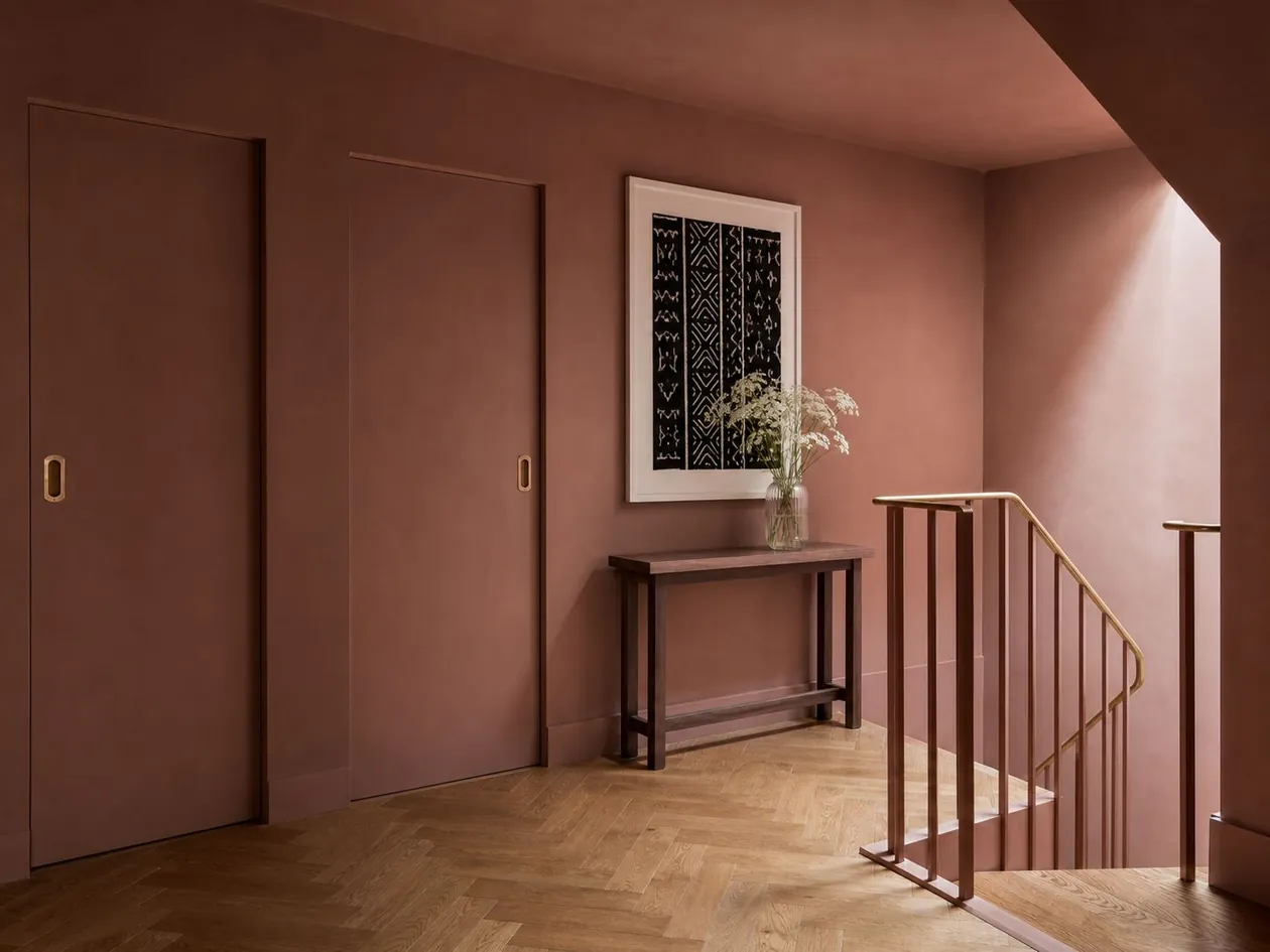 Stair landing drenched in dusty rose with a brass handrail and herringbone parquet — Boutique Hotel