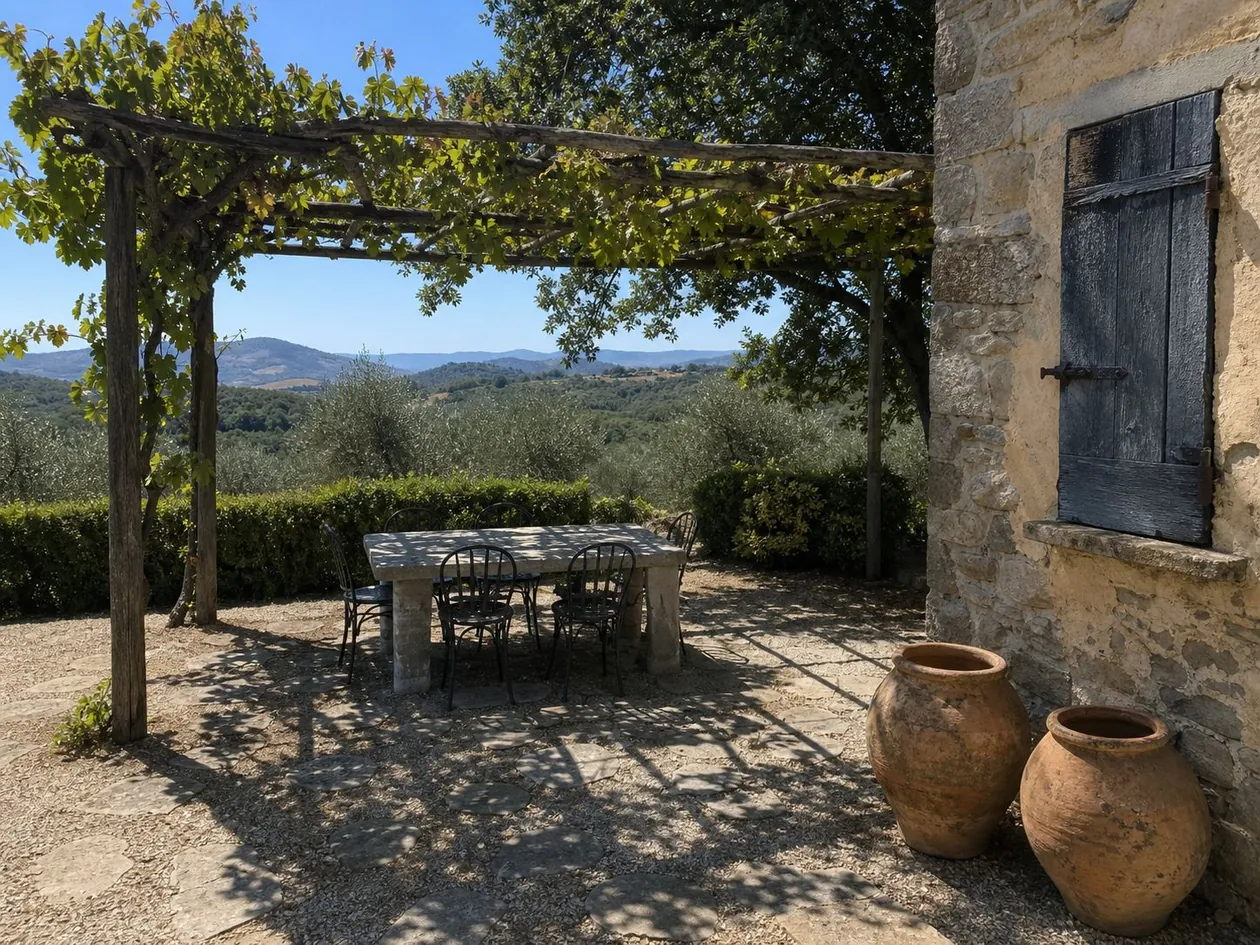 Gravel terrace under a vine pergola, looking out across olive trees to the Tuscan hills — Private Residence, Tuscany